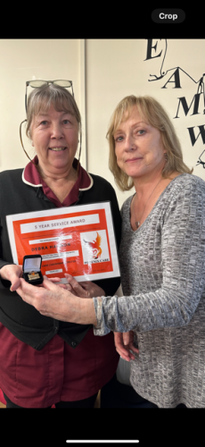 Carer dressed in burgundy uniform receiving a 5-Year service award certificate from her manager.